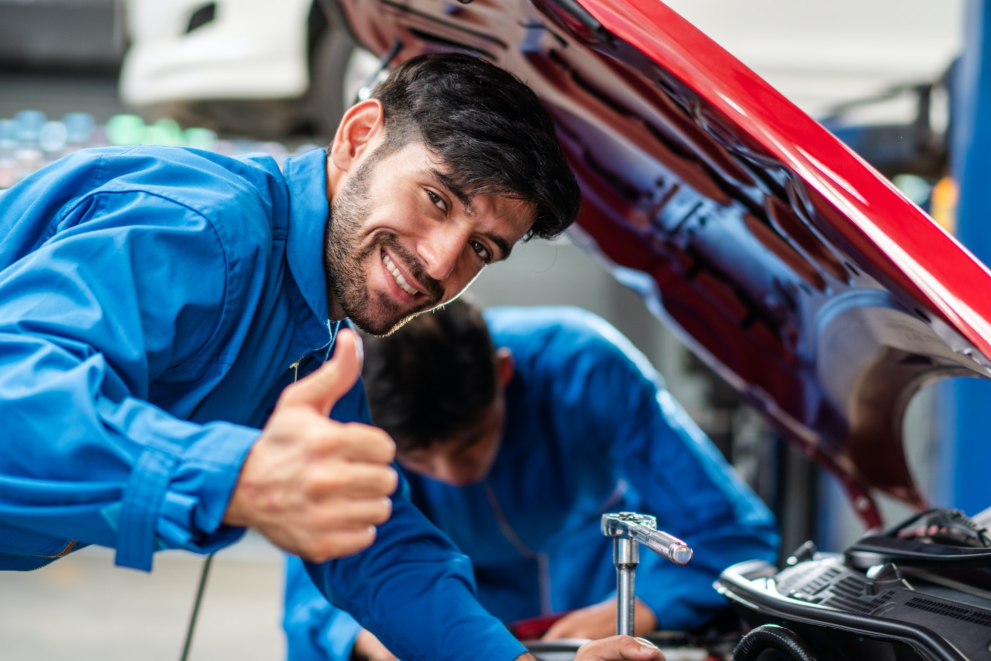 Mechanic showing thumb up while repairing car at auto repair shop